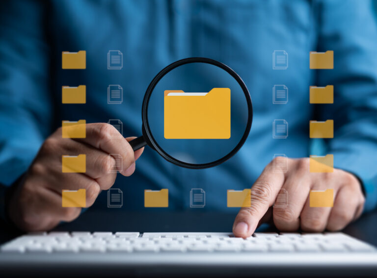 Person using a magnifying glass to search for a folder icon on a computer screen.